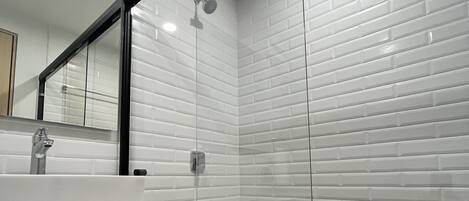 Un baño con azulejos blancos tipo metro, un lavamanos blanco, un espejo y una zona de ducha.