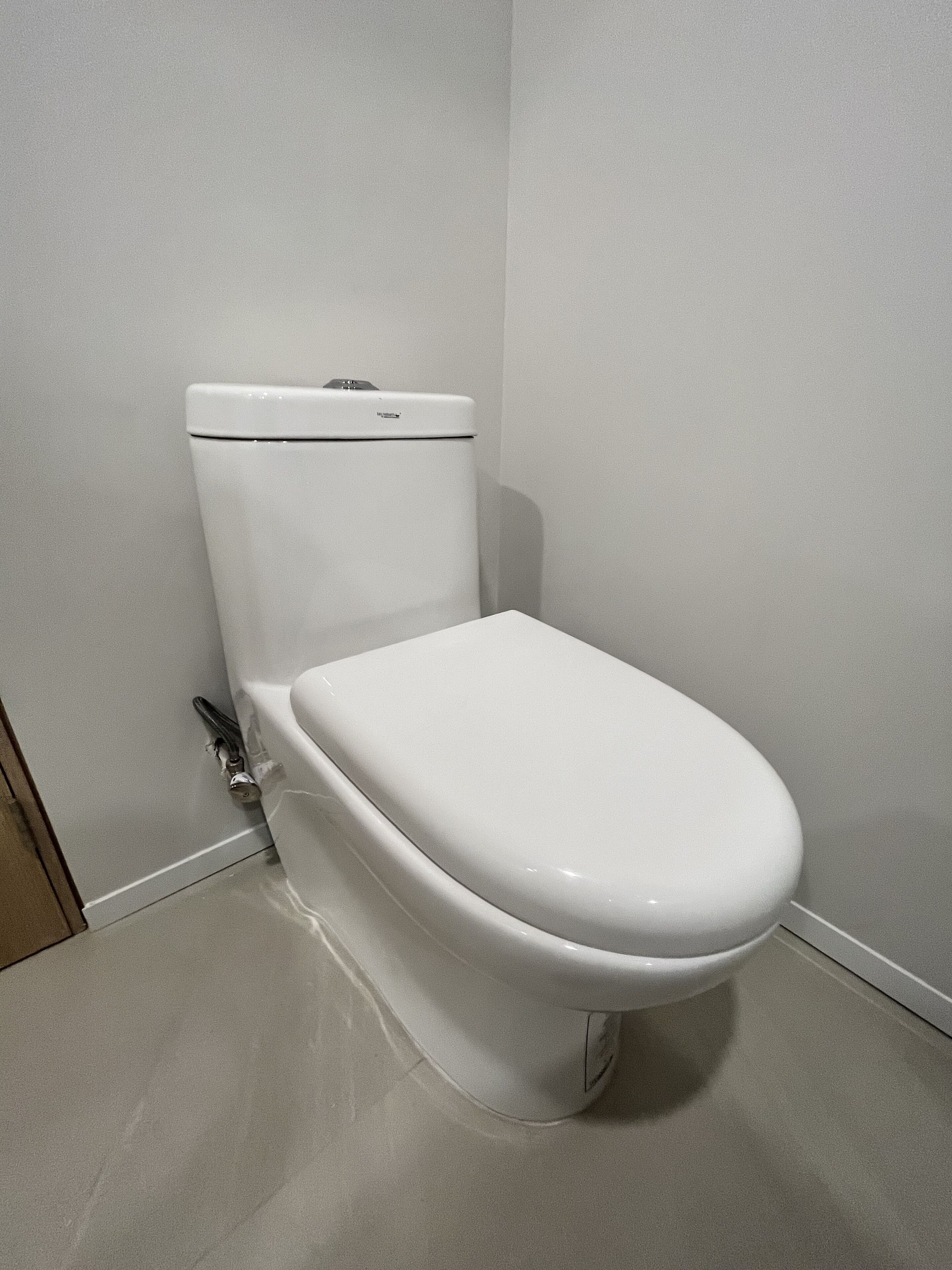 A standard white toilet in a bathroom with a plain wall and a tiled floor.