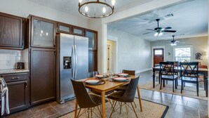 A spacious kitchen with dark wooden cabinets, a stainless steel refrigerator, and a dining area with a wooden table and chairs. - Chic Lawton Home, 5 Mins to Fort Sill! (Lawton)