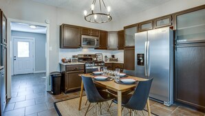 A modern kitchen with stainless steel appliances, wooden cabinets, and a dining area with a table set for four. - Chic Lawton Home, 5 Mins to Fort Sill! (Lawton)