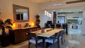 A modern dining area with a large table, chairs, and a kitchen in the background.