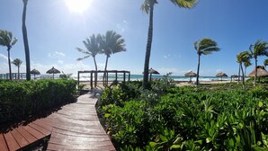 A wooden pathway leading to a beach with thatched umbrellas and palm trees.