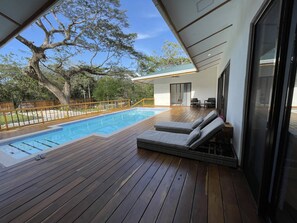Una terraza de madera con piscina, sillas de descanso y vistas del paisaje circundante.