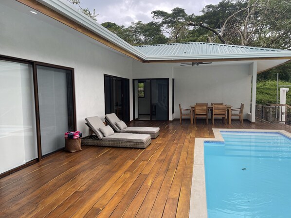 Una terraza de madera con piscina, sillas de descanso y una mesa.