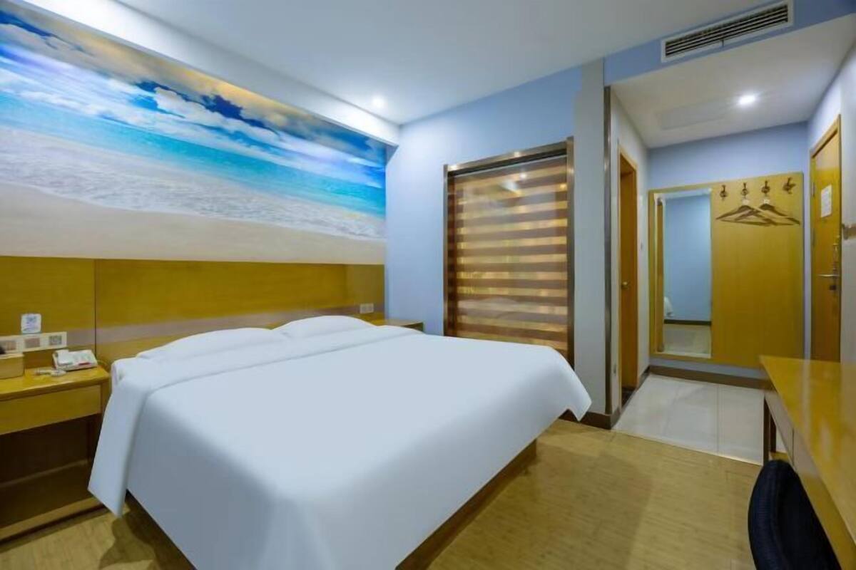 A hotel room with a bed, a desk with a phone, a mirror, and a door with a coat rack.