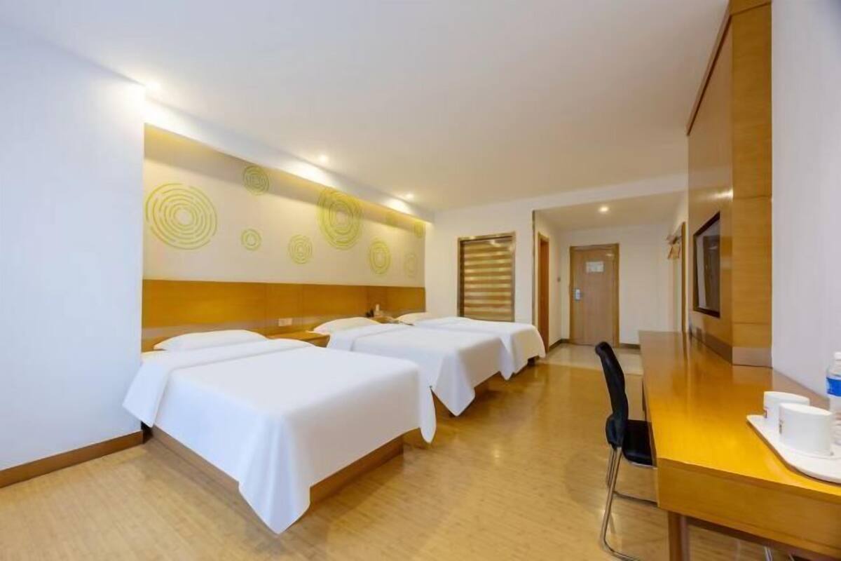A hotel room with three beds, a wooden desk, and a television.