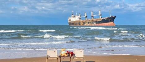 Una playa con un banco y un barco al fondo.