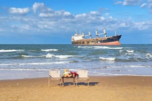 Una playa con un banco y un barco al fondo.