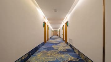 Ein Hotelkorridor mit einem gemusterten Teppich, Wandleuchten und einem Deckenlüfter.