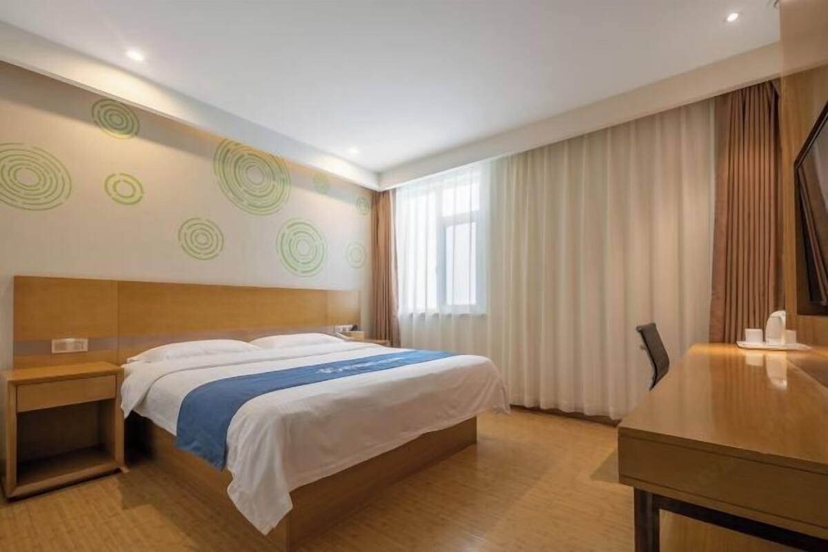 A hotel room with a large bed, a wooden nightstand, a desk, and a window with curtains.