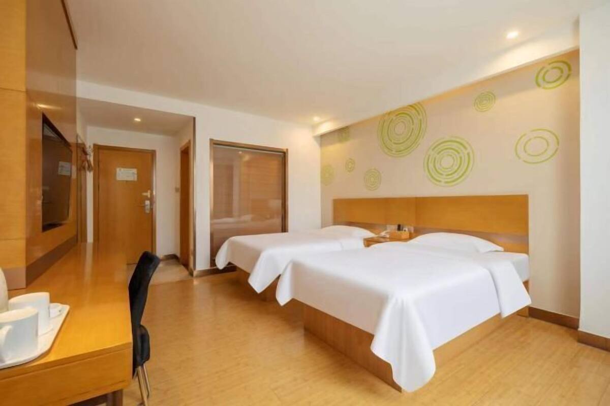 A hotel room with two beds, a wooden desk, and a mirror.