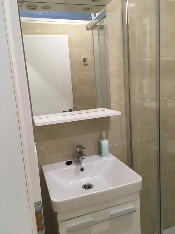 Un baño con lavamanos blanco, un espejo y una cabina de ducha con paredes de vidrio.