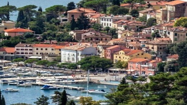 Un pueblo costero con un puerto deportivo, edificios históricos y abundante vegetación.