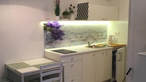 Cocina compacta con encimera blanca, un lavamanos, un refrigerador pequeño y una zona de comedor con una silla y mesa.