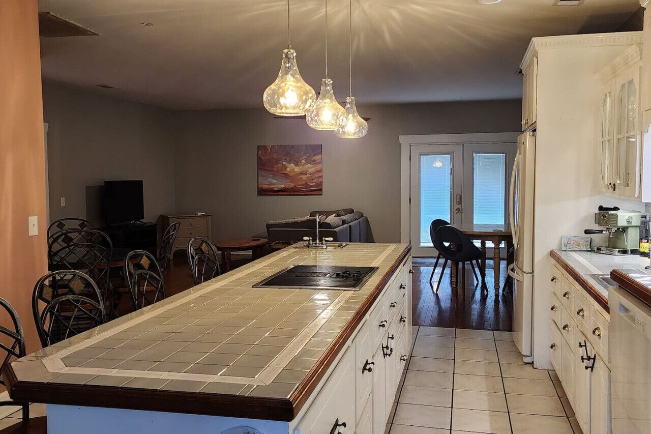 A kitchen with a central island, pendant lights, and a dining area with chairs and a table.
