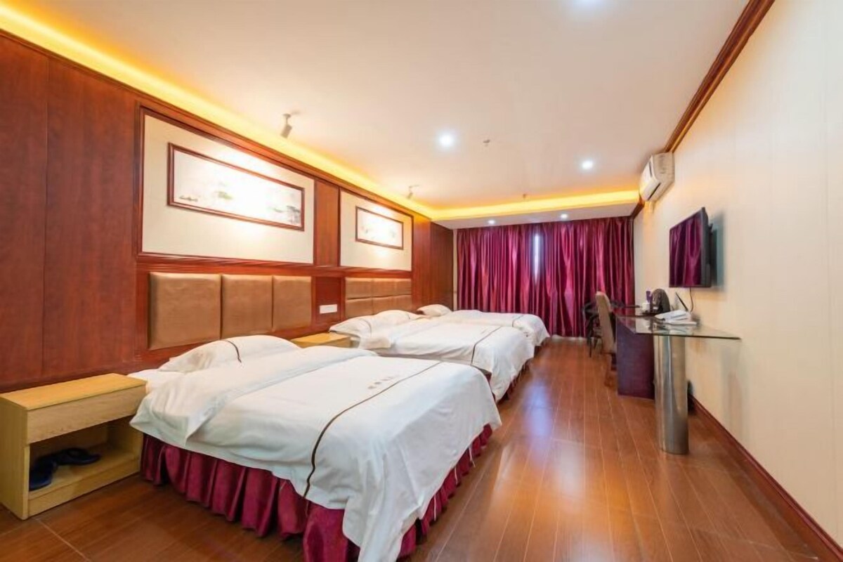 A hotel room with three beds, wooden paneling, a desk, and a television.