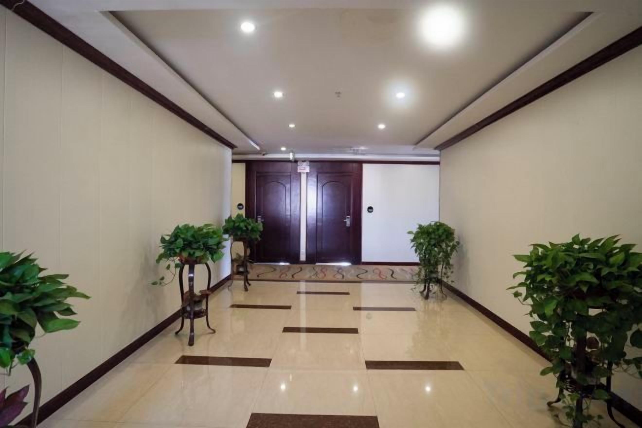 A hotel lobby with a tiled floor, two potted plants, and a double door at the end.