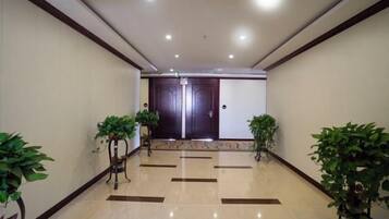 A hotel lobby with a tiled floor, two potted plants, and a double door at the end.