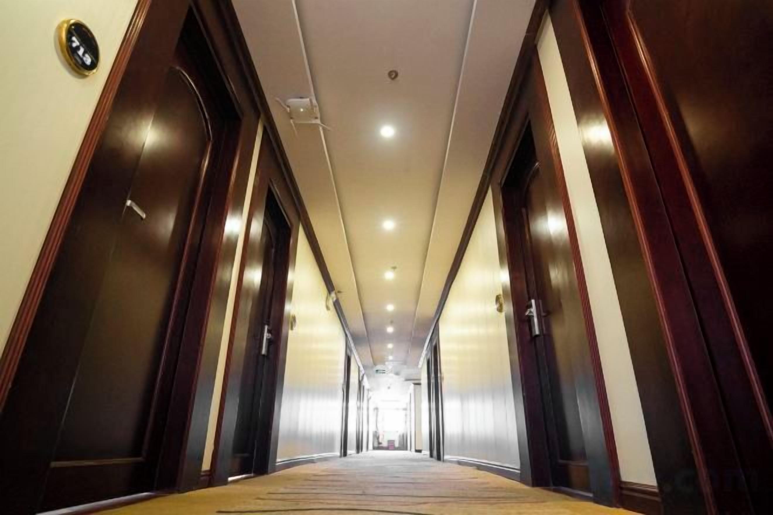 A hotel corridor with doors on both sides, a carpeted floor, and a ceiling with recessed lighting.
