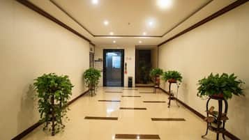 A hotel corridor with a tiled floor, potted plants, and a door at the end.