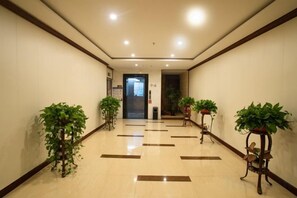 Pasillo de hotel con piso de baldosas, plantas en macetas y una puerta al final.