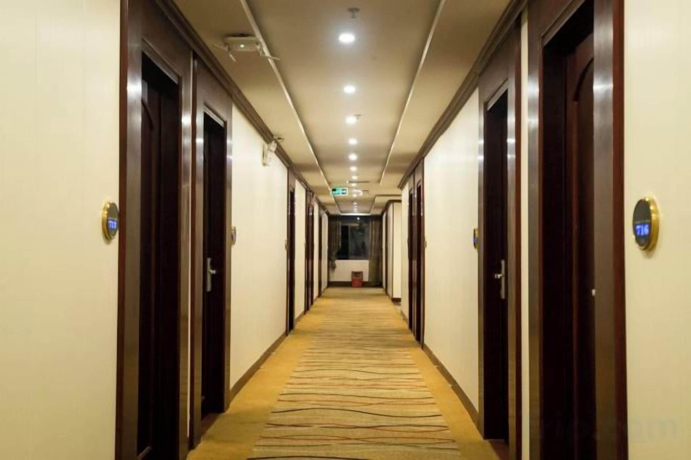 A hotel corridor with doors on both sides, a carpeted floor, and a ceiling with recessed lighting.