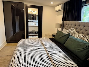 Quarto com cama, mesa de cabeceira, luminária, espelho, guarda-roupa e ar condicionado.