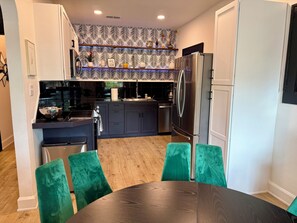 A modern kitchen with dark cabinets, a stainless steel refrigerator, and a dining area with green chairs.