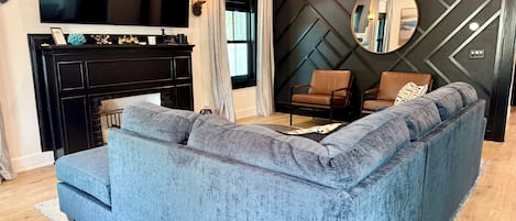A modern living room with a blue sofa, a fireplace, a TV, and a decorative wall.