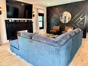 A modern living room with a blue sofa, a fireplace, a TV, and a decorative wall.