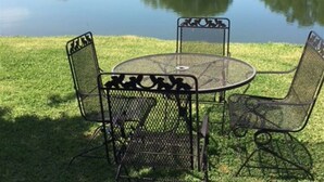 A round metal table with chairs in a grassy area near a body of water. - Country Cabin  10 miles from Round Top (Burton)