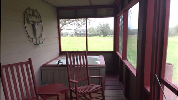 A porch with two rocking chairs and a small table, a window with a view of a grassy field, and a wall-mounted sculpture. - Country Cabin  10 miles from Round Top (Burton)