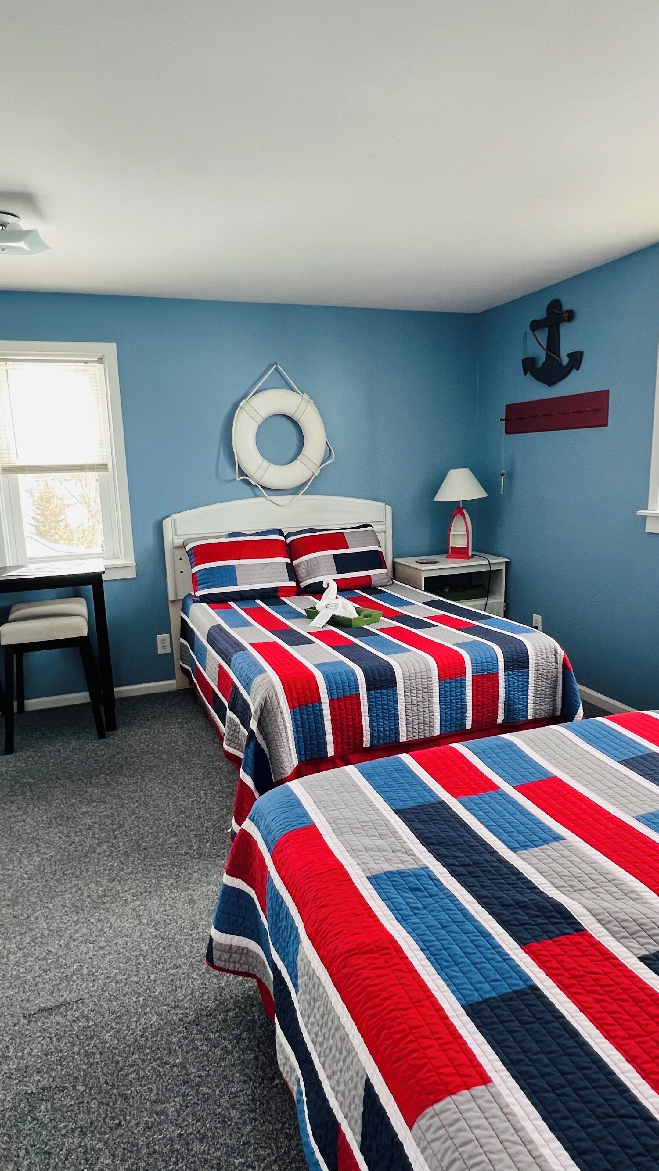 A bedroom with two beds, a window, a nightstand, a lamp, and a wall decoration.