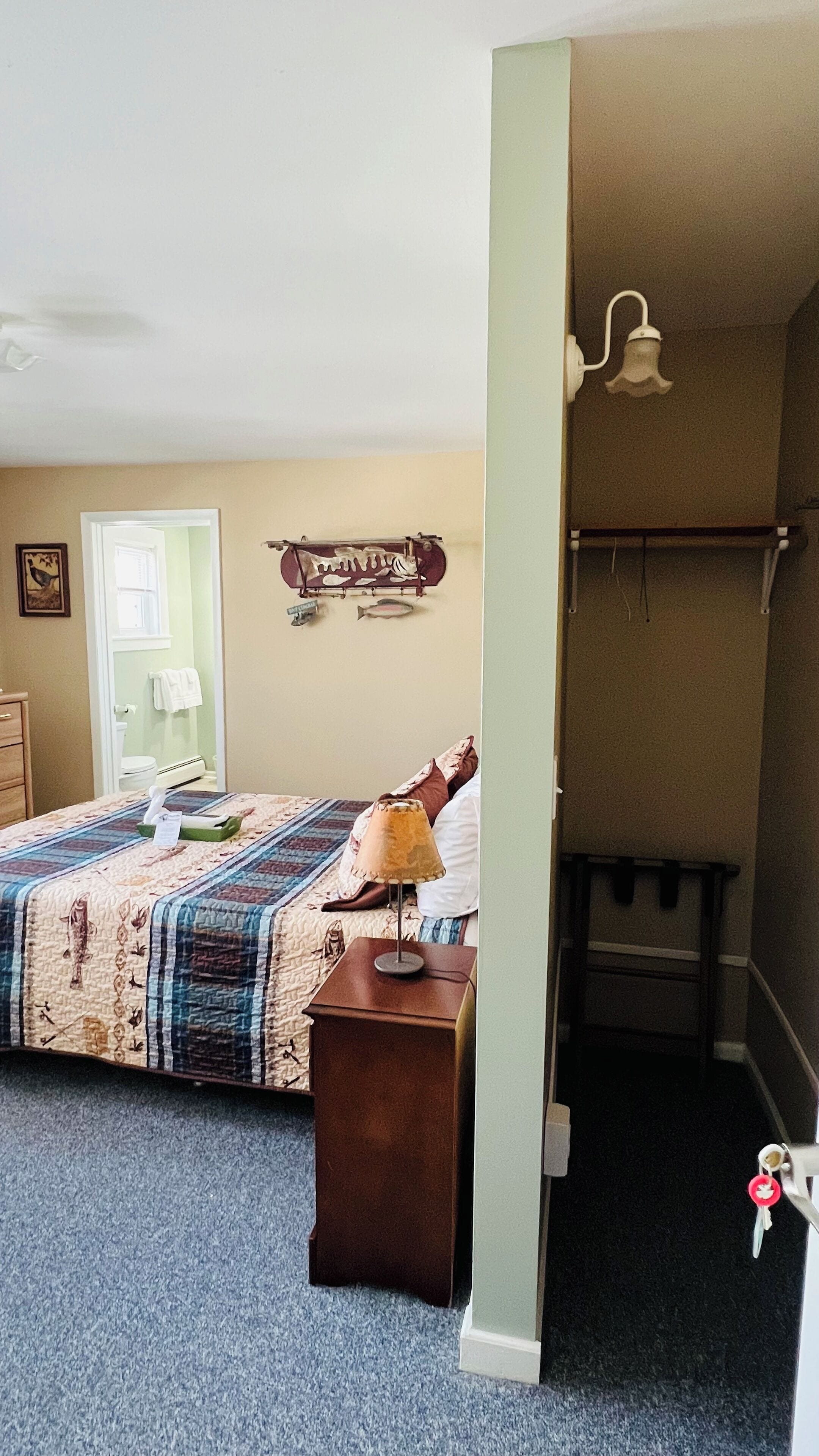 A bedroom with a bed, a nightstand, a lamp, and a wall-mounted shelf with a fish decoration.
