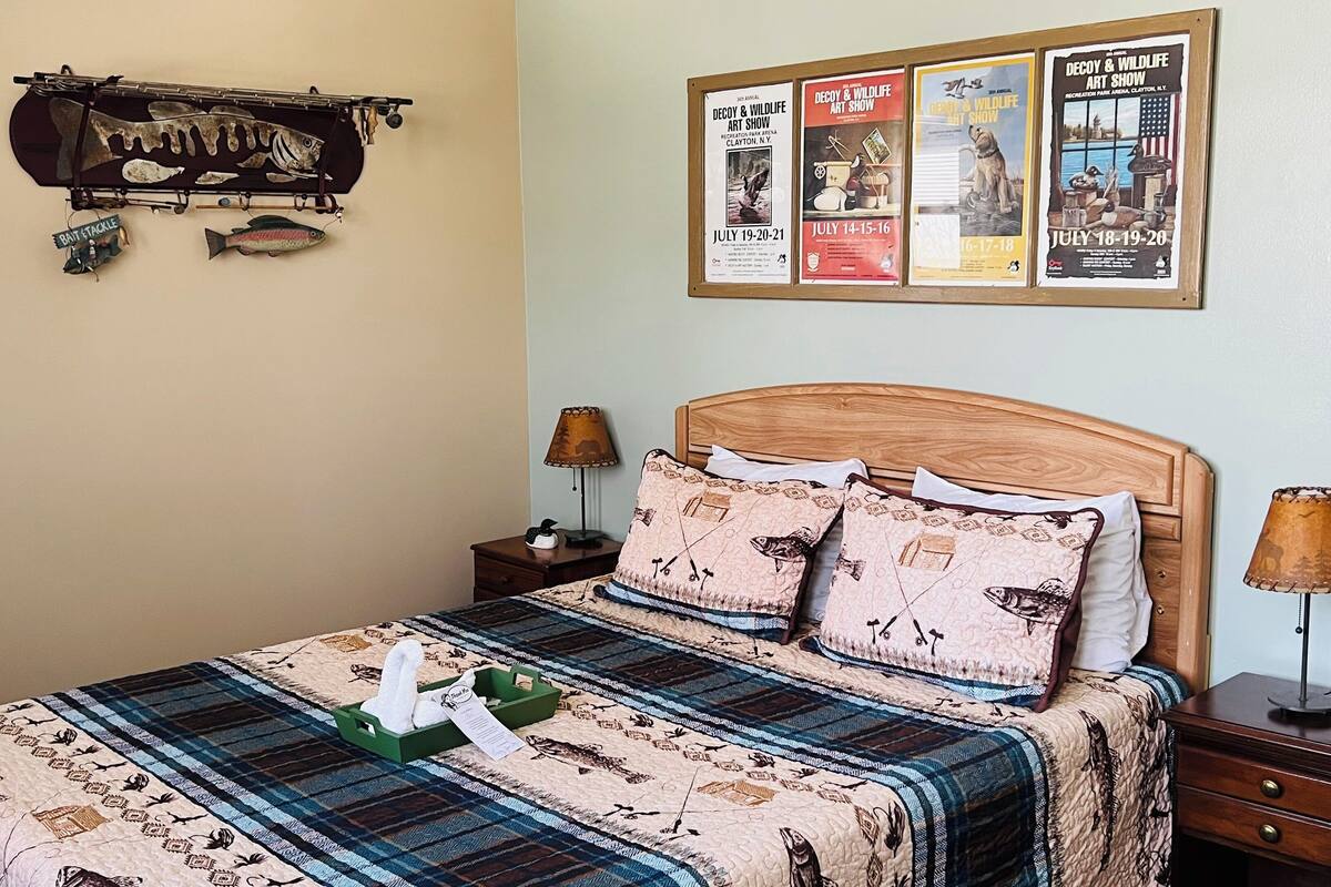 A neatly arranged bedroom with a bed, two nightstands, a wall-mounted fish rack, and three posters advertising art shows.