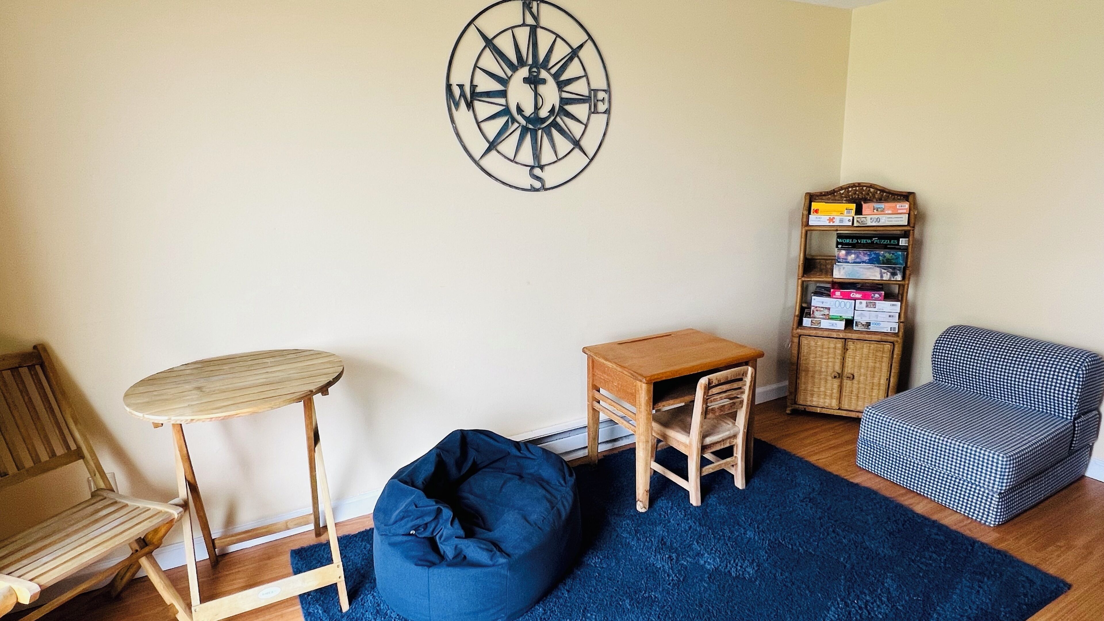 A cozy room with a wooden table, a blue bean bag, a bookshelf, and a patterned chair.
