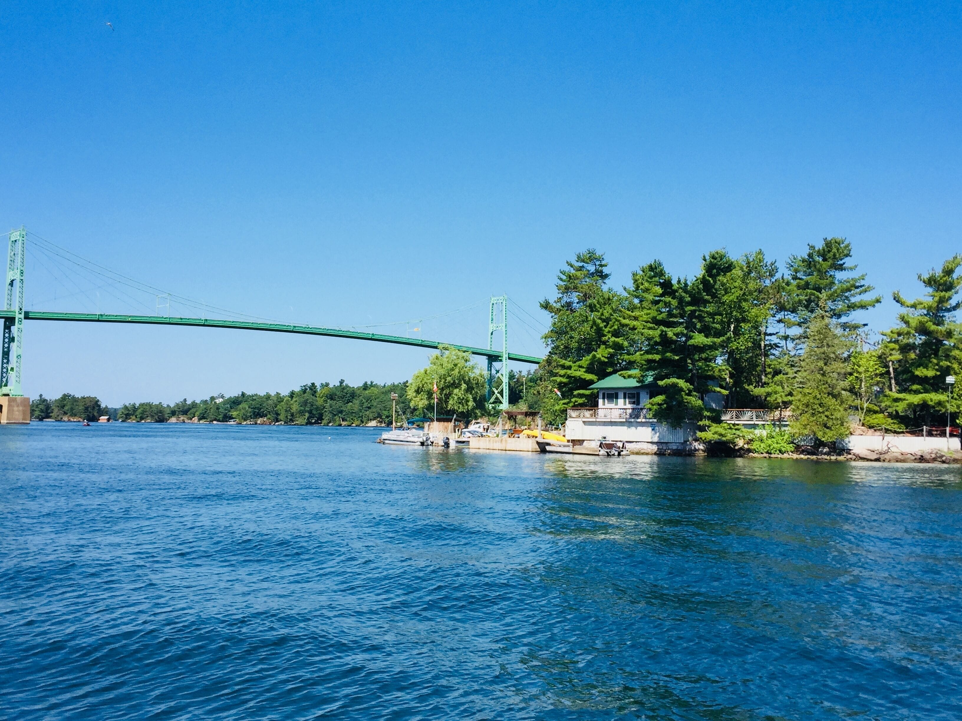A river with a green bridge, a dock with boats, and a house with a green roof near the water.