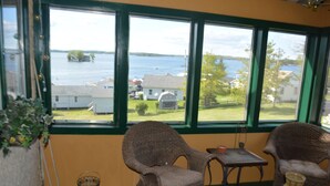 A room with a view of a lake, wicker chairs, a small table, and a basket. - Chateau Country Inn  (Clayton)