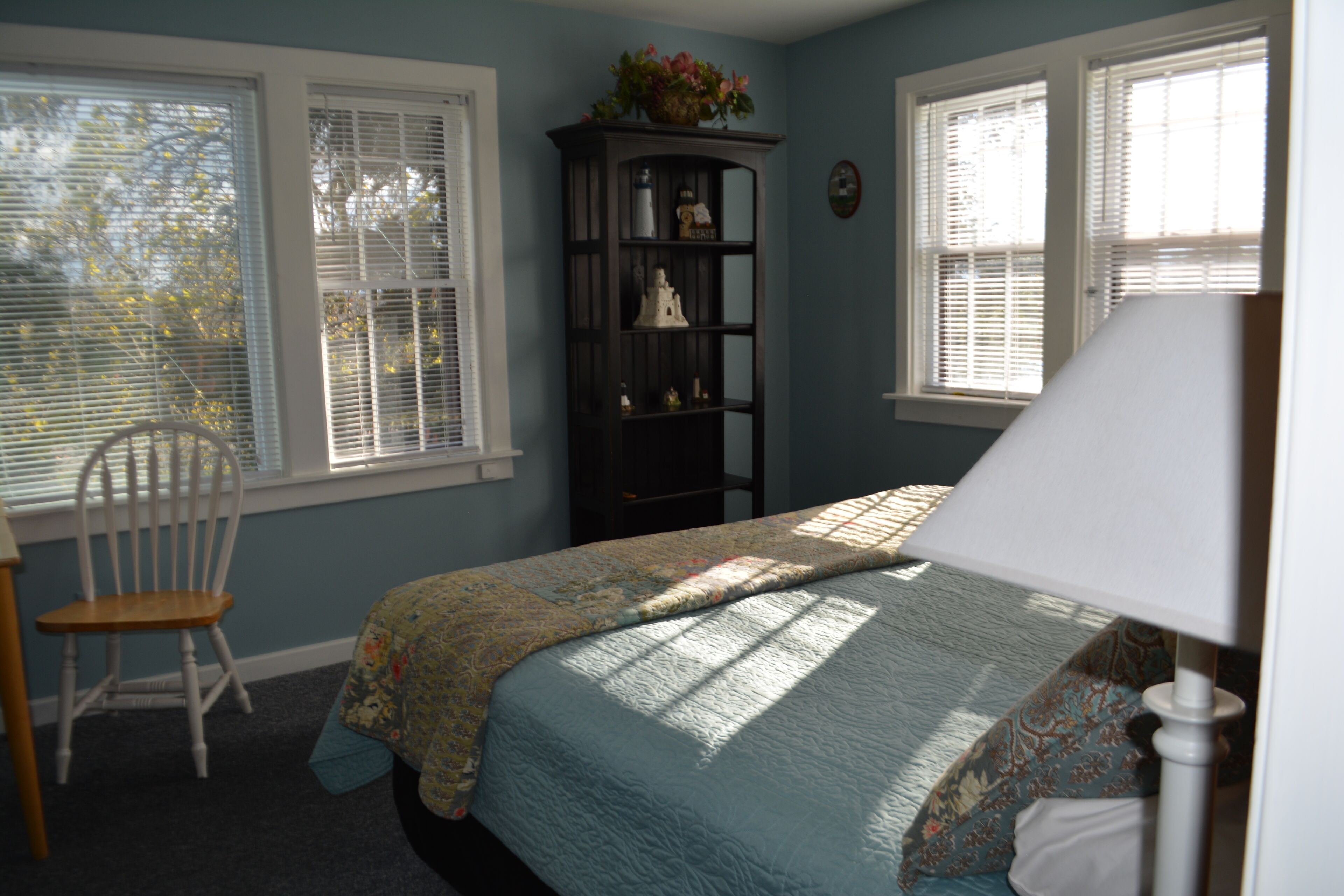 A bedroom with a bed, a chair, a nightstand, and a window with blinds.