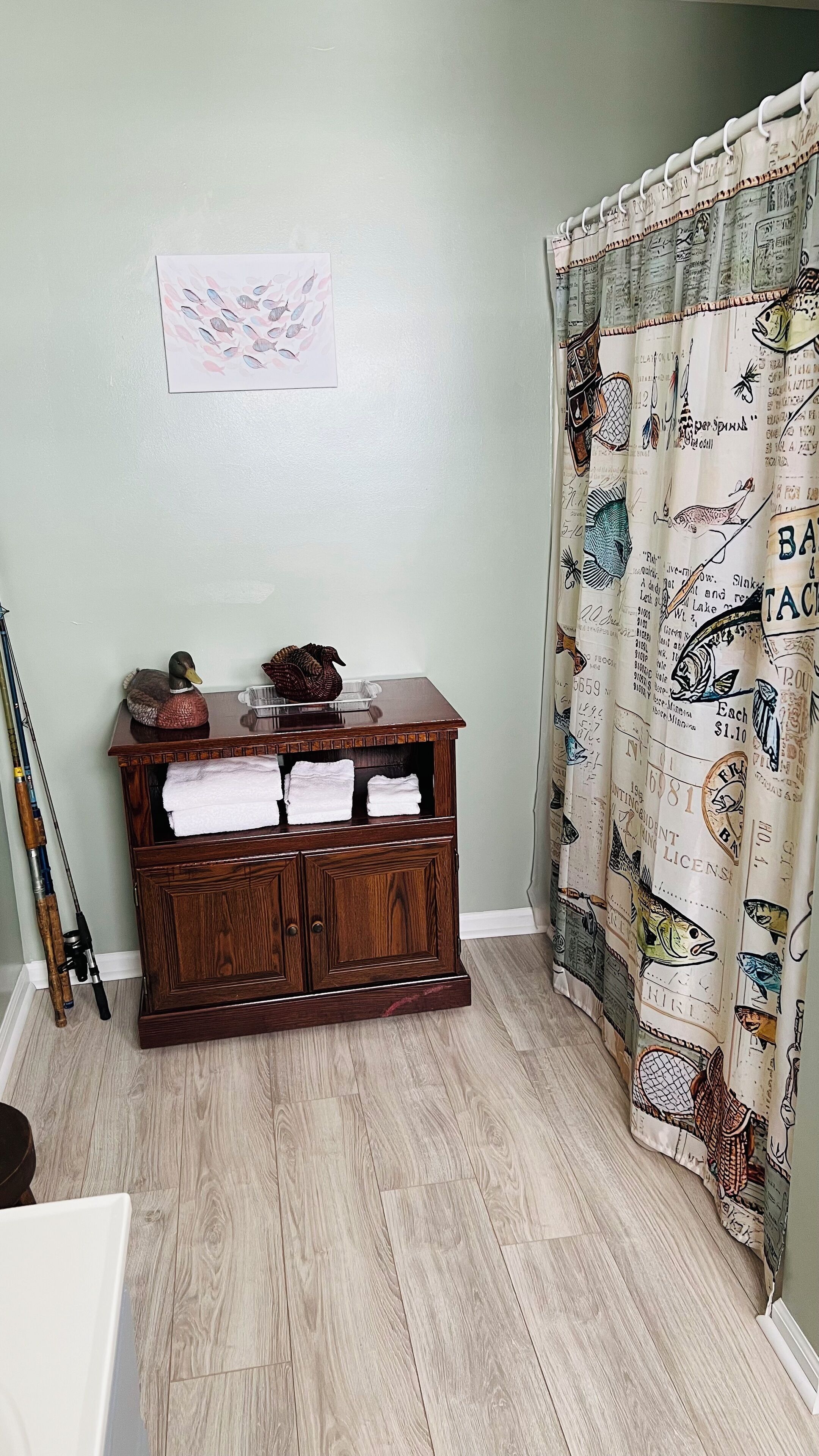 A room with a wooden cabinet, fishing rods, and a curtain with fish illustrations.