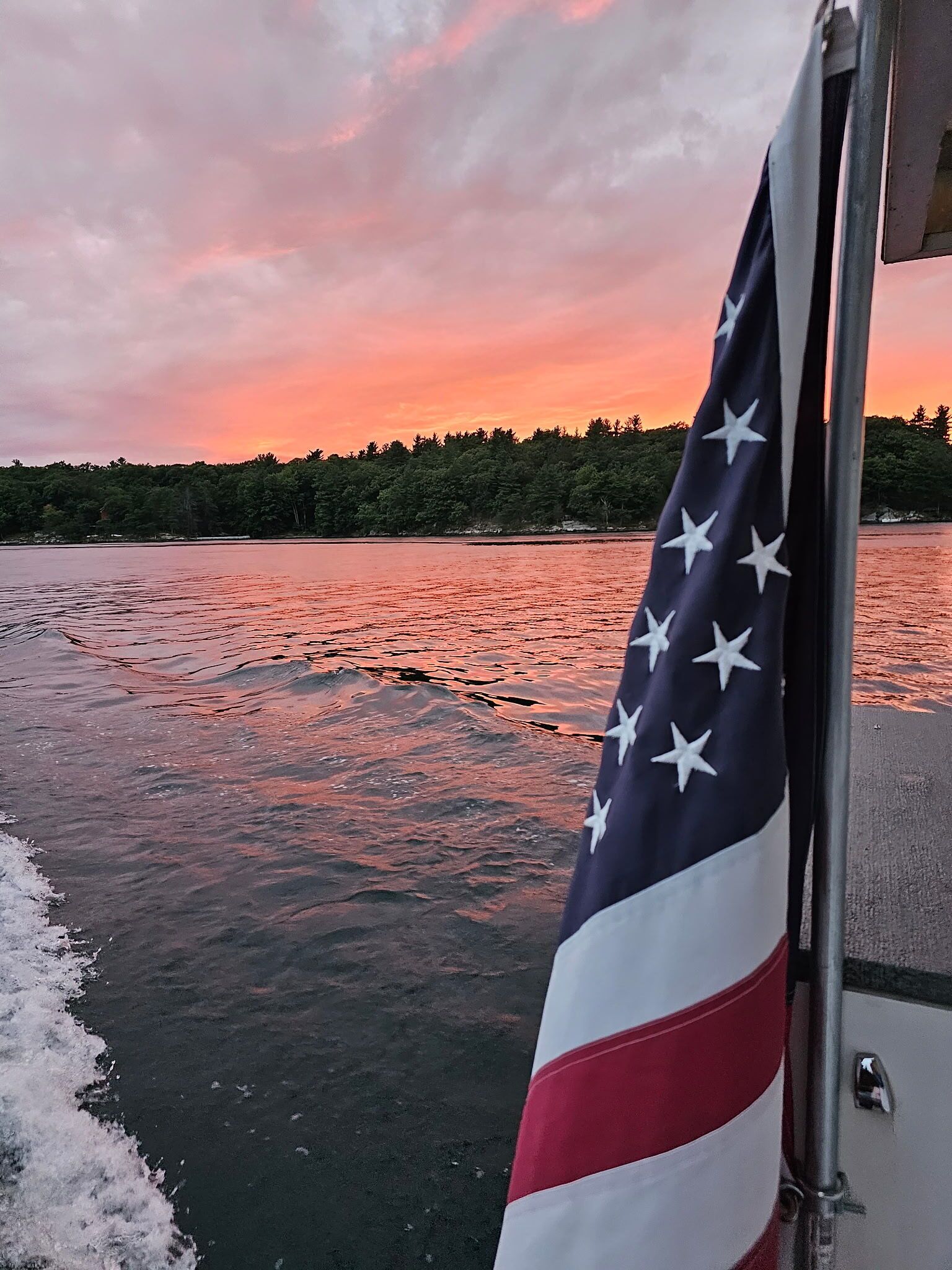 Una bandera en un barco con vista a la costa boscosa al atardecer.