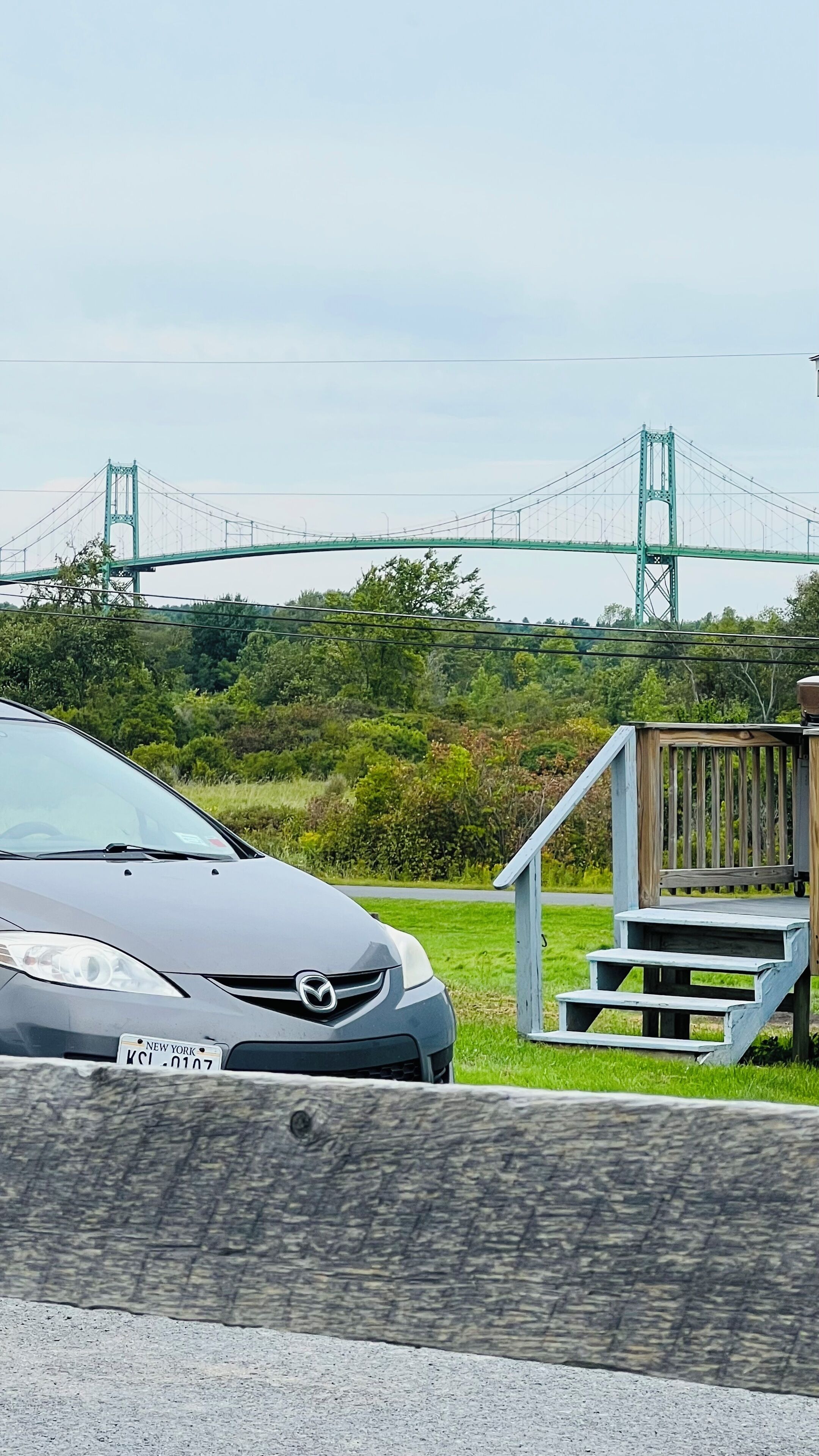 A car parked near a wooden staircase leading to a deck, with a bridge in the background.