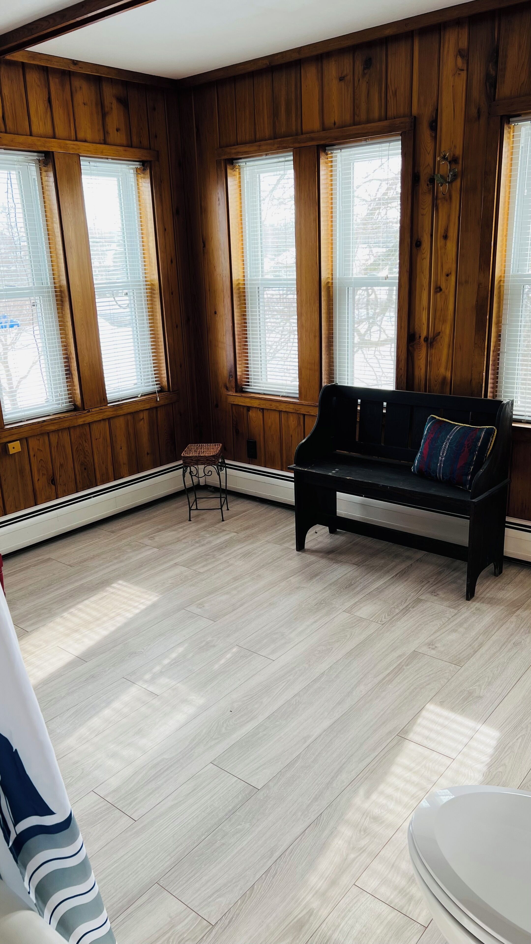 A room with wooden paneled walls, a black bench with a cushion, a wicker chair, and a radiator.