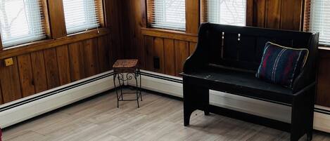 A room with wooden paneled walls, a black bench with a cushion, a wicker chair, and a radiator.