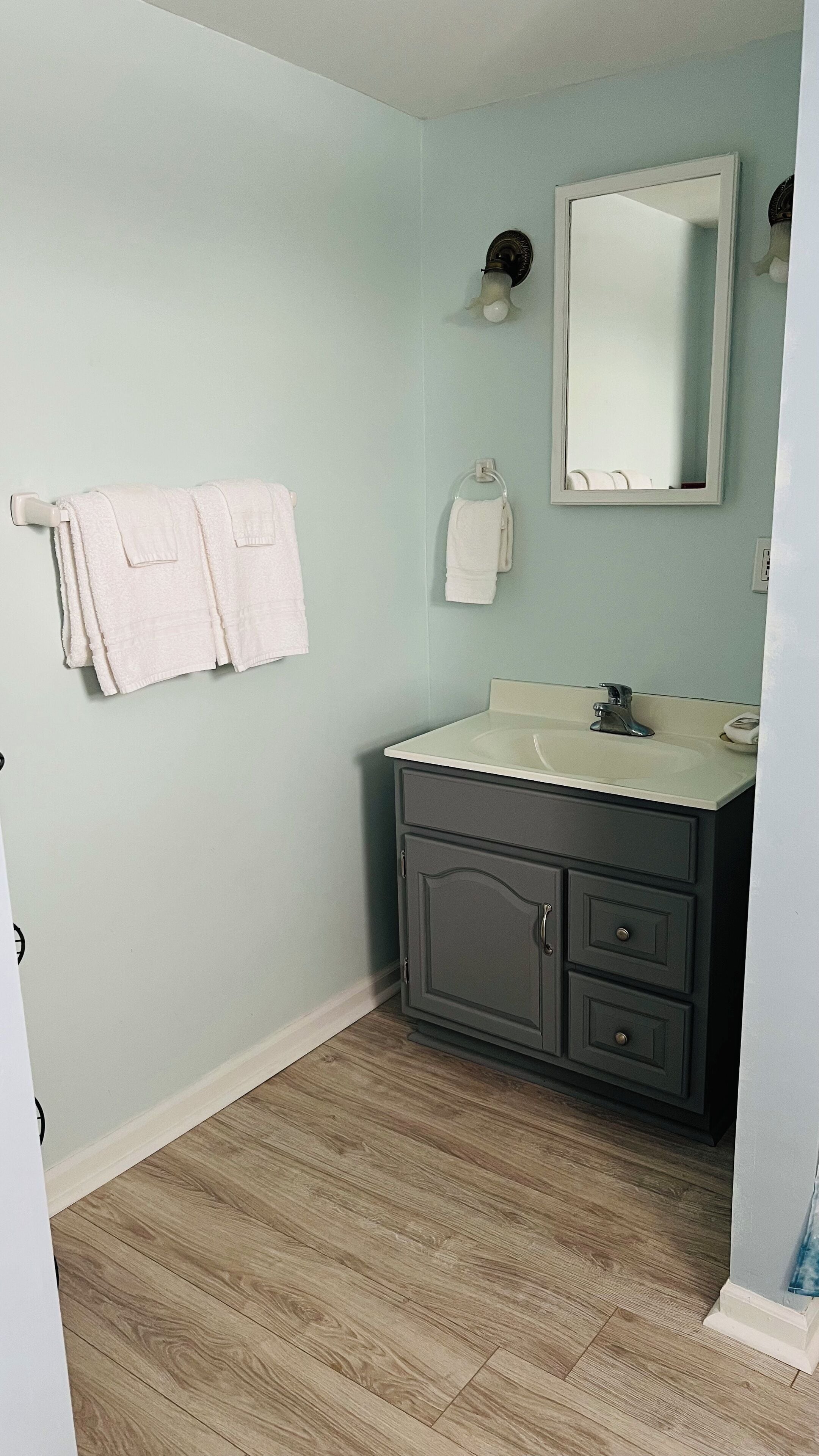 A bathroom with light green walls, a white sink, and a dark cabinet. There are two white towels hanging on hooks.