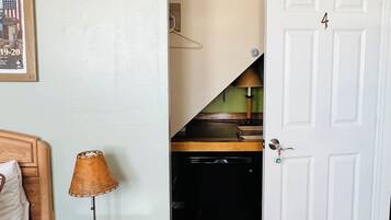 A bedroom with a bed, a nightstand with a lamp, a door, and a desk with a chair.