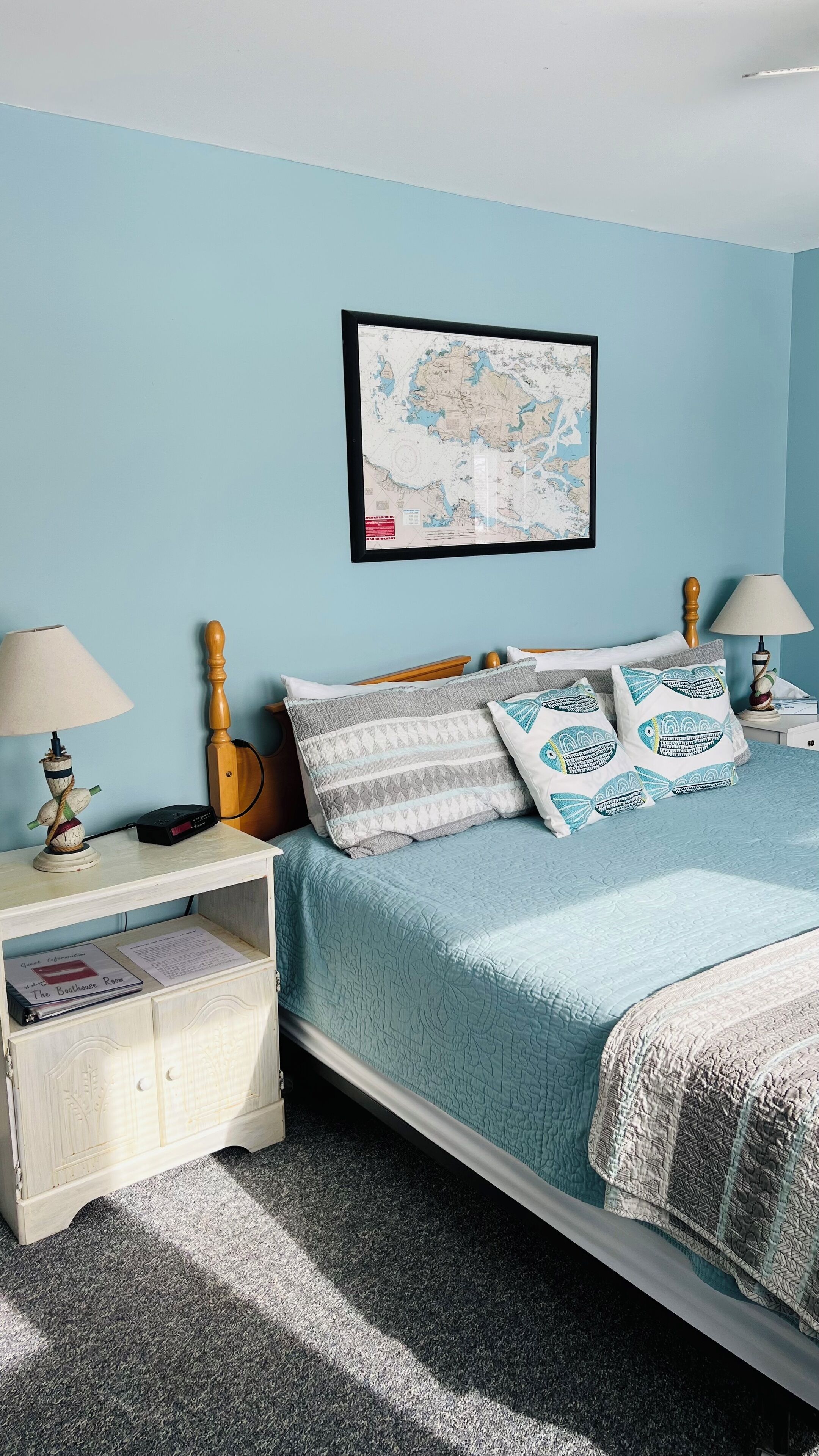 Un dormitorio con cama, dos mesitas de noche, un mapa en la pared y un pequeño armario de madera.