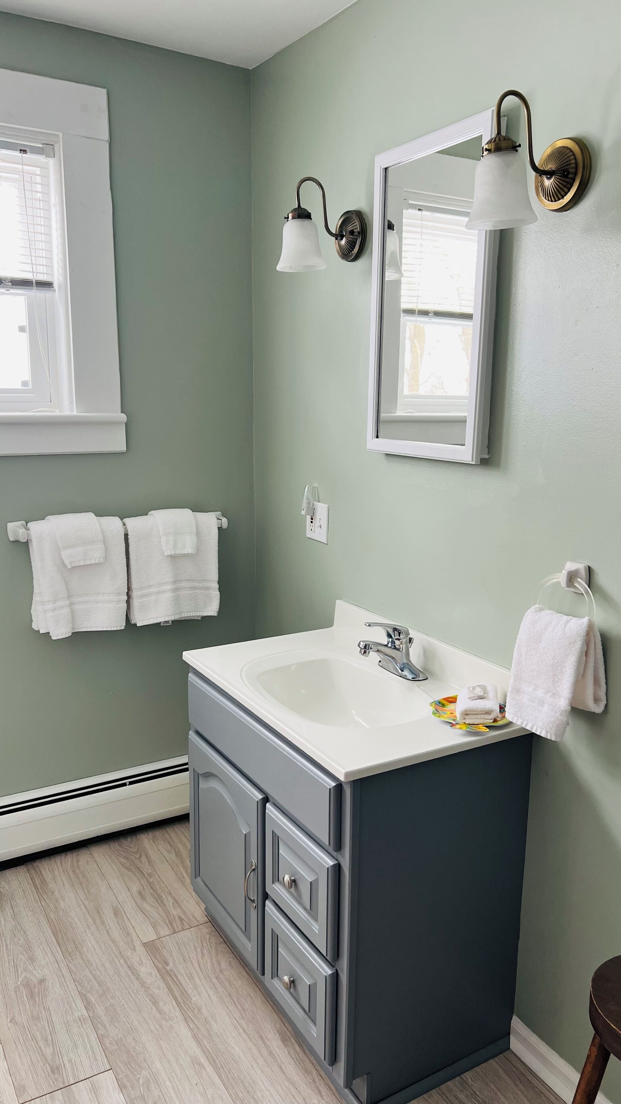 A bathroom with a white sink, dark cabinets, and a light green wall. There are two white towels hanging on the wall and a towel on the counter.