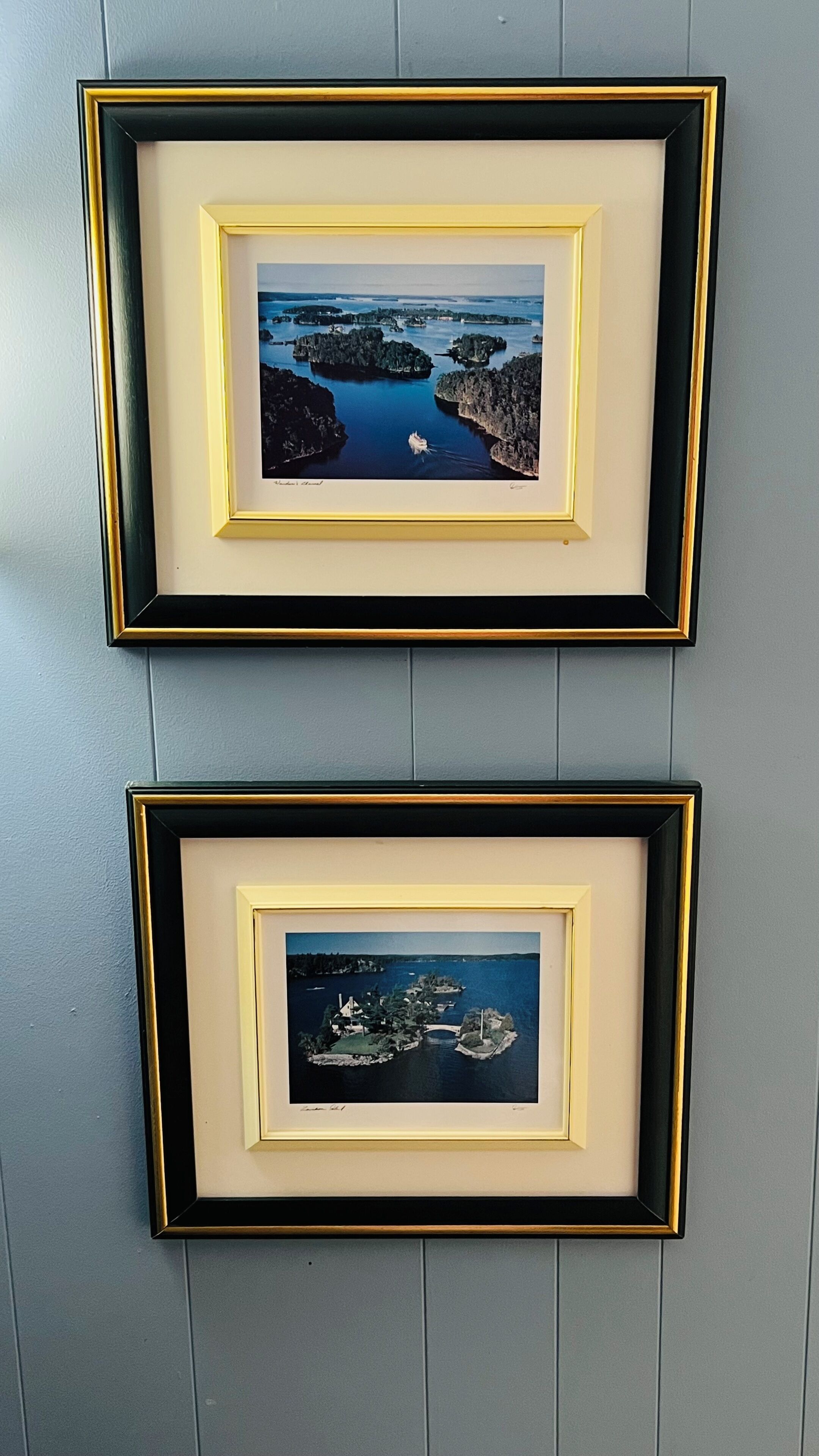 Two framed photographs of coastal landscapes with boats, mounted on a wall with vertical paneling.