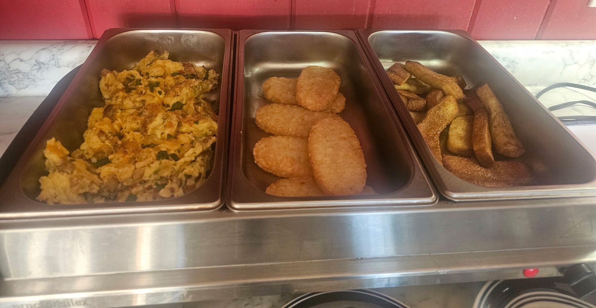 Trois plateaux contenant des œufs brouillés, des galettes de viande frites et des frites.